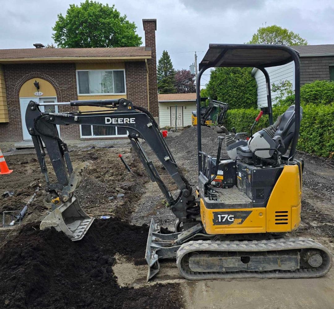 Une mini-excavatrice John Deere de Location Lalancette devant une résidence